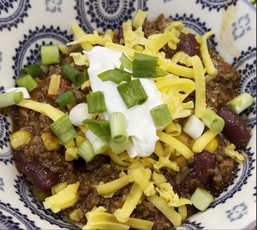 A colorful bowl of chili with grated cheese, sour cream, and green onions